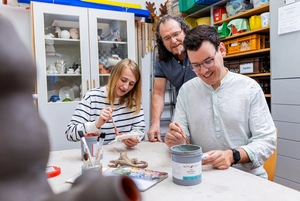 Ein Mann und eine Frau betätigen sich kreativ und ein weiterer Mann schaut ihnen über die Schultern Ein Mann und eine Frau betätigen sich kreativ und ein weiterer Mann schaut ihnen über die Schultern