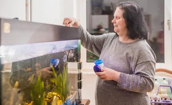 Frau füttert Fische im Aquarium Frau füttert Fische im Aquarium